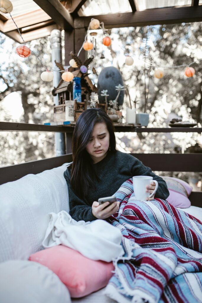 Woman wrapped in blanket, holding coffee, relaxing on patio.