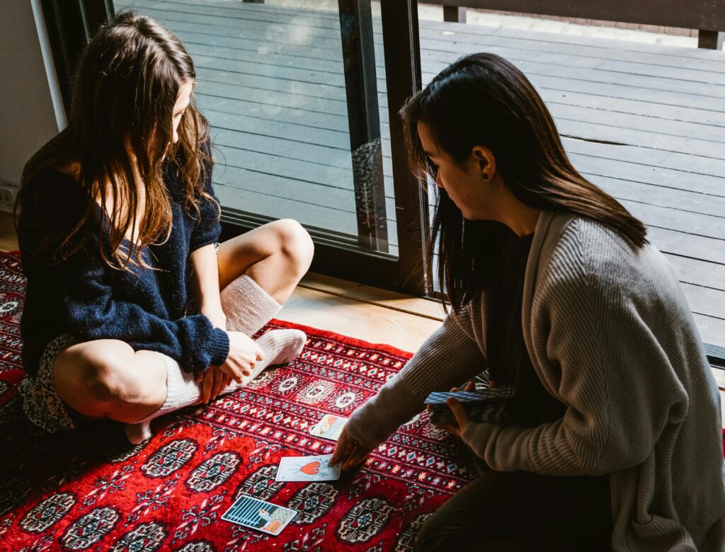 Two women engaged in a tarot reading session on a cozy indoor rug, reflecting relaxation and introspection.